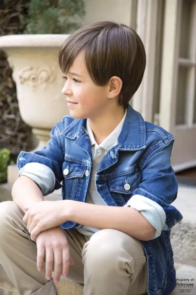 A boy sitting on the ground wearing a jean jacket.