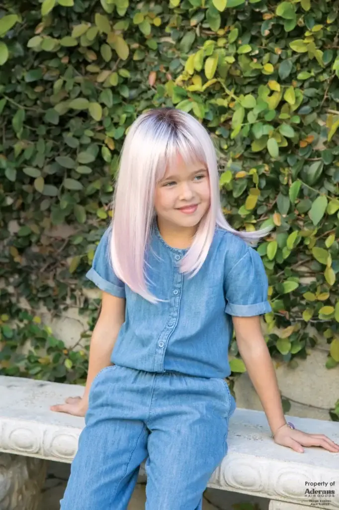 A young girl with long blonde hair sitting on the ground.