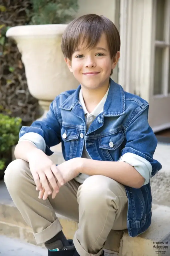 A young boy sitting on the ground wearing jeans.