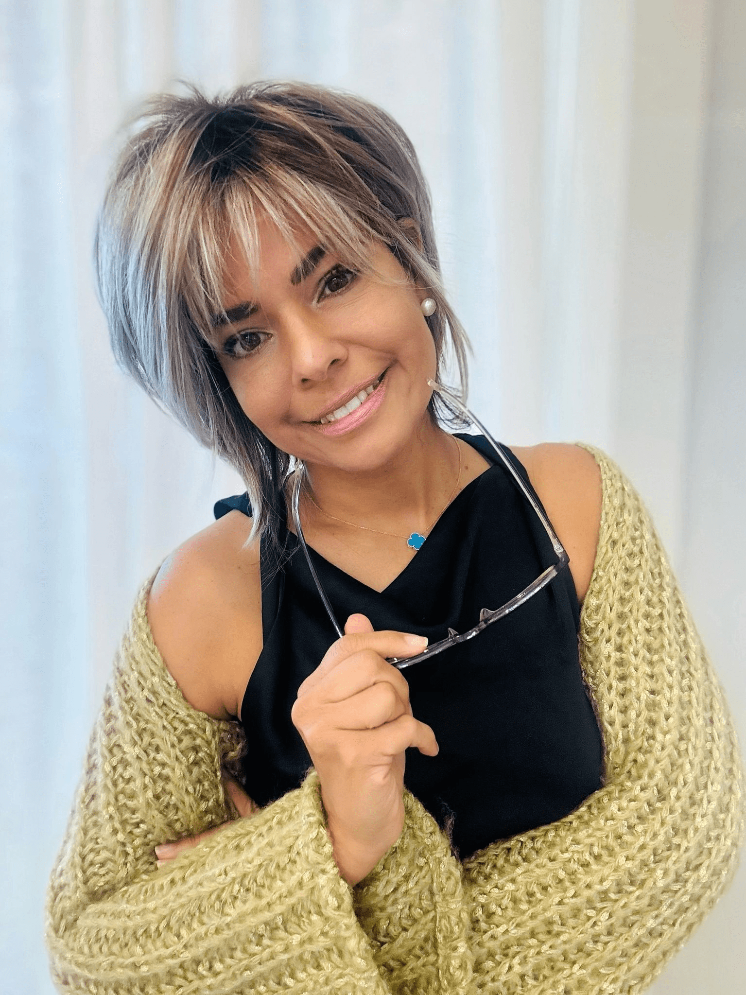 A woman holding her glasses and smiling for the camera.