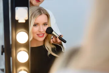 A woman is holding a makeup brush in front of her face.