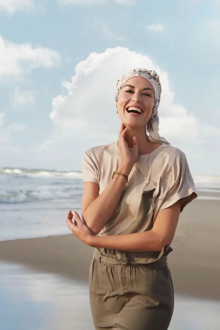 A woman standing on the beach with her hands under her chin.