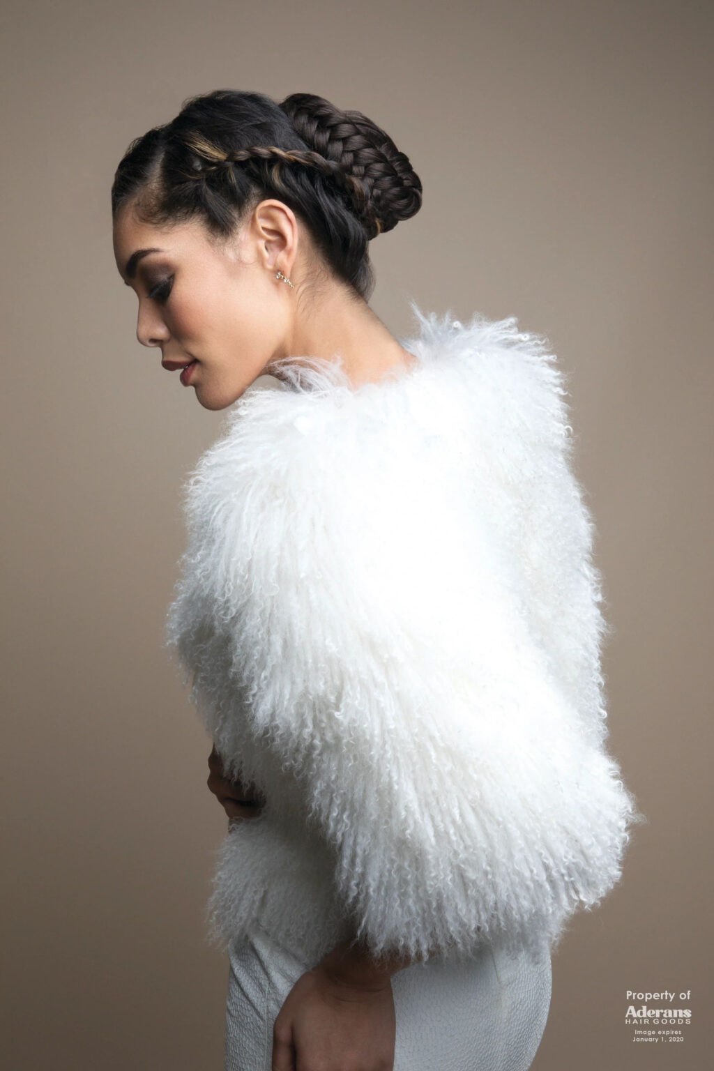 A woman in white fur jacket standing next to wall.