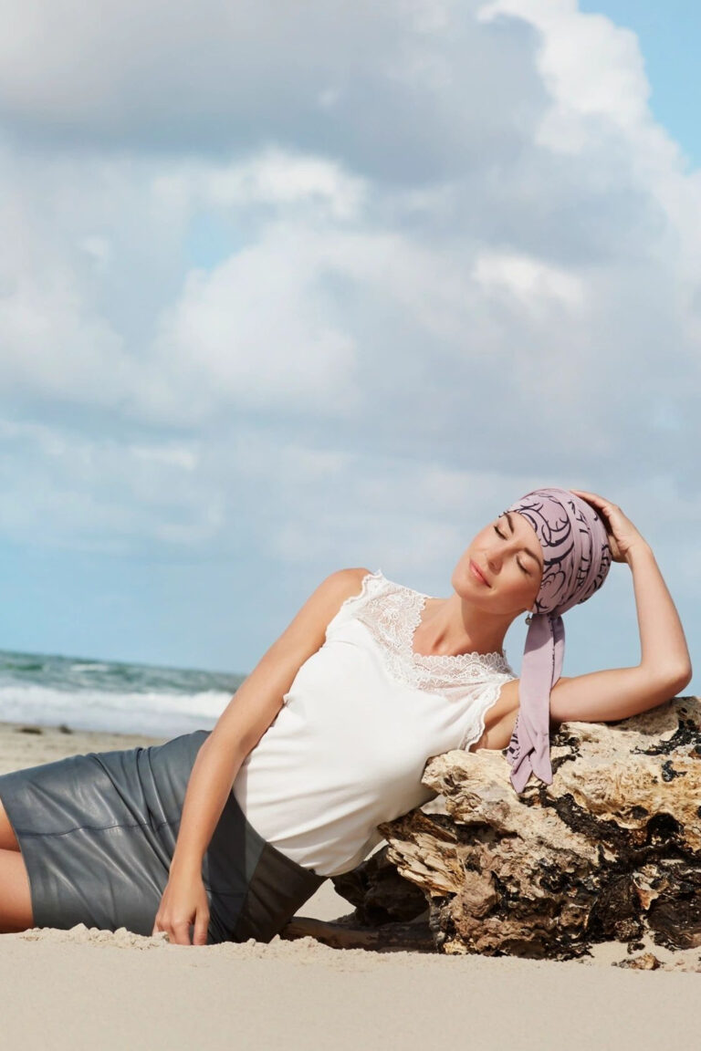 A woman laying on the beach with her head wrapped in a scarf.